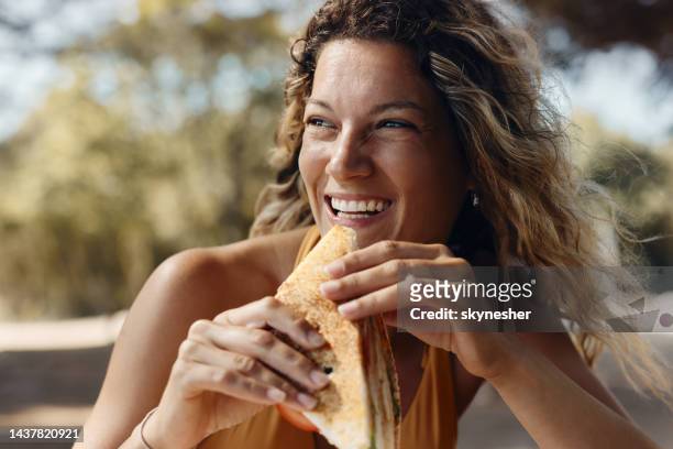 happy woman eating a sandwich in summer day. - woman sandwich stock pictures, royalty-free photos & images