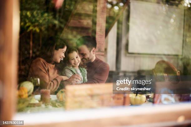 happy parents enjoying with their daughter at dining table. - photographed through window stock pictures, royalty-free photos & images