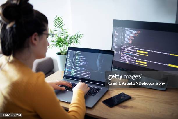female programmer using laptop and computer while sitting at desk at home office. - female programmer stock pictures, royalty-free photos & images