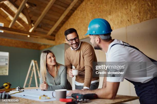 feliz pareja hablando con un trabajador manual en el sitio de construcción. - contratista de obras fotografías e imágenes de stock
