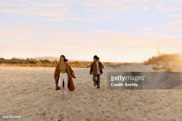 madre e hija corriendo en la playa en invierno - mothers day beach fotografías e imágenes de stock