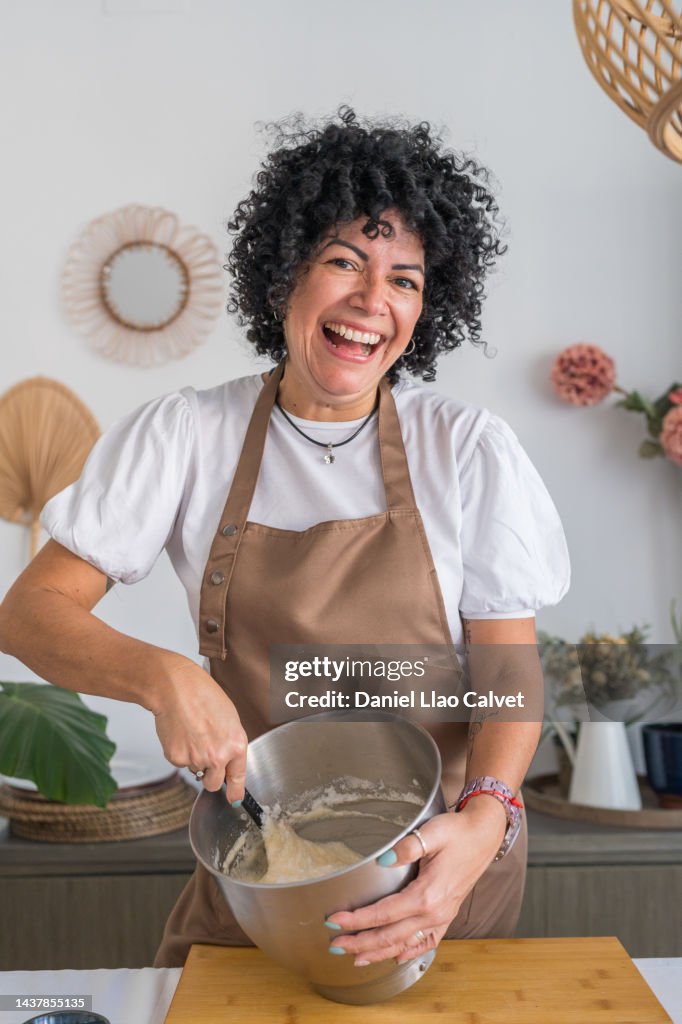 Happy Latin woman stirring batter in kitchen