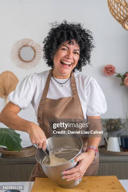 happy latin woman stirring batter in kitchen - pasteleiro imagens e fotografias de stock