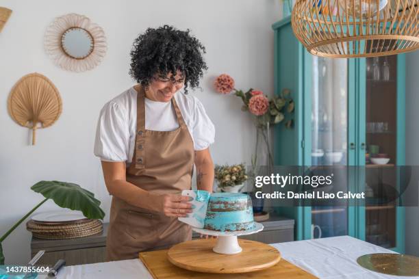 latin woman spreading whipped blue cream over chocolate cake in the kitchen - decorating a cake stock pictures, royalty-free photos & images