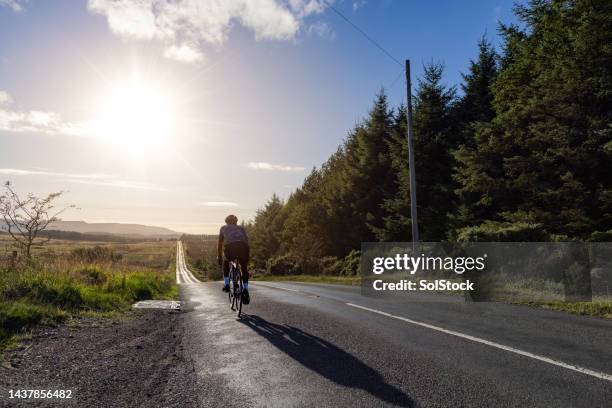 cycling alone on long road - wielrennen stockfoto's en -beelden