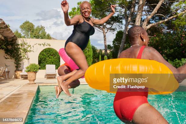 a small group of women jumping into a villa swimming pool - images of black families stock-fotos und bilder