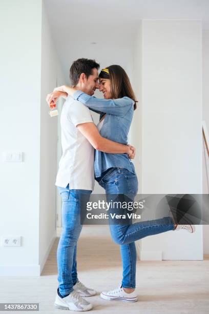 caucasian couple expecting baby kissing decorating new house white background. - vita domestica fotografías e imágenes de stock