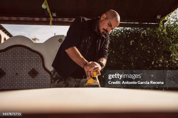 a 40-year-old man sands his table top on the patio with an electric sander - sandblasting stock pictures, royalty-free photos & images