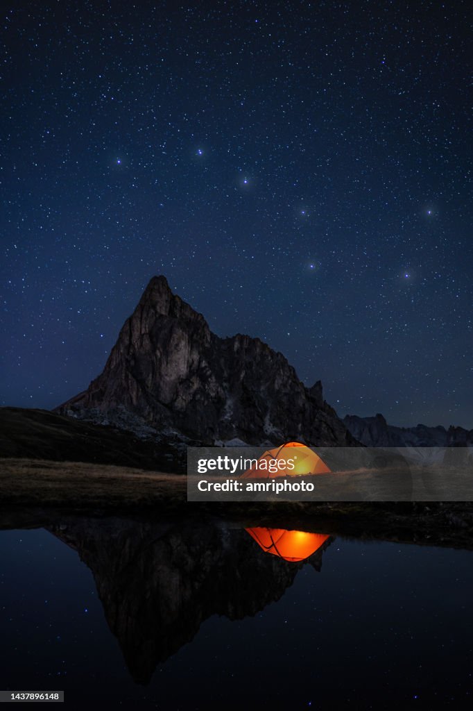 Constelación de estrellas Big Dipper sobre el pico de la montaña, el lago y la tienda iluminada con reflejos en aguas tranquilas