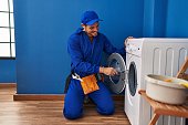 Young hispanic man technician repairing washing machine at laundry room
