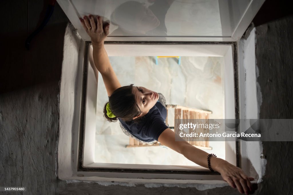 Woman peeks through the hatch of the stairs to the attic
