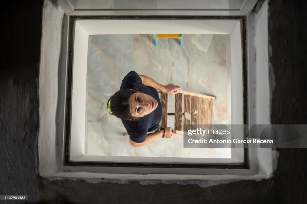 Woman peeks through the hatch of the stairs to the attic