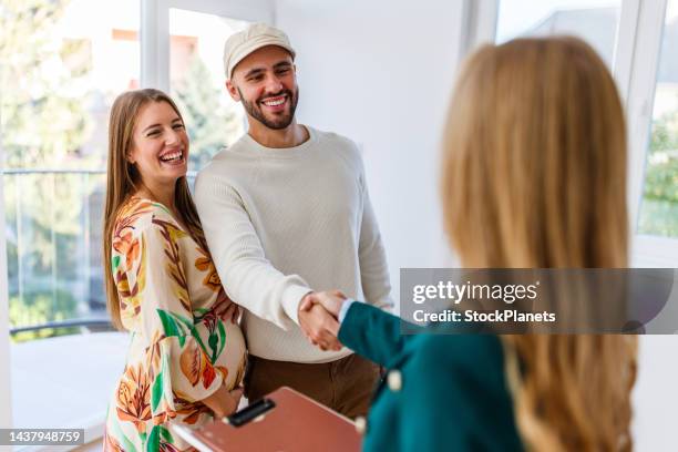 young happy couple, a pregnant woman, and an agent shaking hands in a new property - pregnant women greeting stockfoto's en -beelden