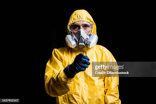 portrait of technician wearing yellow nuclear protection suit, mask and goggles, pointing finger at camera. concept of nuclear energy and pandemics. - hazardous workplace stock-fotos und bilder