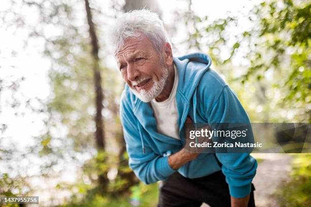 senior man athlete having heart problems during jogging - heart attack stockfoto's en -beelden