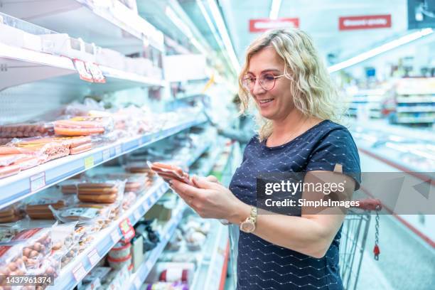 a woman buys sausages in a grocery store, checks the expiration date. - meat product stock pictures, royalty-free photos & images