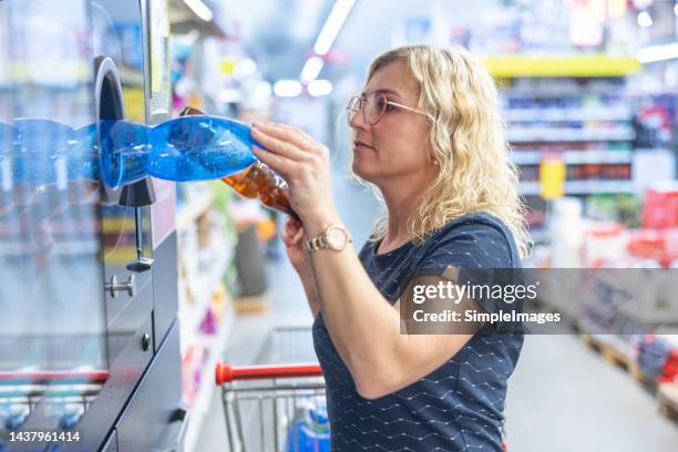 a grocery store customer puts an empty plastic bottle into the recycling machine. - devolución del saque fotografías e imágenes de stock
