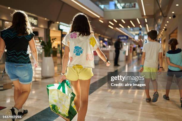 woman with children walking down the aisle in the mall at the side of the stores, rear view, girl carrying shopping bag - shopping imagens e fotografias de stock
