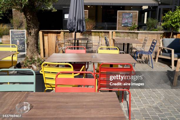 restaurant or cafe with wooden tables outdoors with no people on a sunny day, one tree and black umbrella on the side, front view - patio table stock pictures, royalty-free photos & images