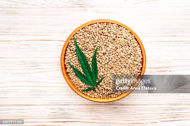 cannabis leaf and hemp seeds in bowl on wooden background. concept of using healthy food supplements. photography from above - hemp seed fotografías e imágenes de stock