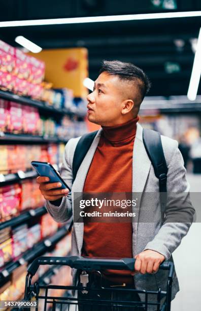 handsome asian male searching for groceries from the list on his mobile phone - food technology stock pictures, royalty-free photos & images