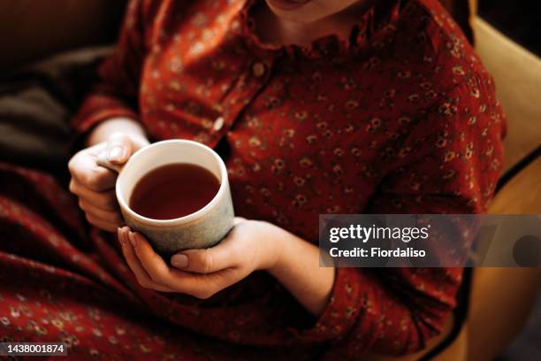 portrait of a long-haired red-haired woman sitting on the sofa with cup of tea - black tea stock pictures, royalty-free photos & images