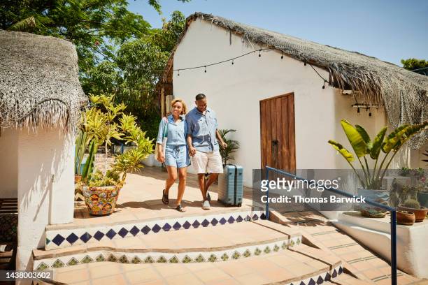wide shot of couple walking into tropical resort while on vacation - suitcase couple stock-fotos und bilder