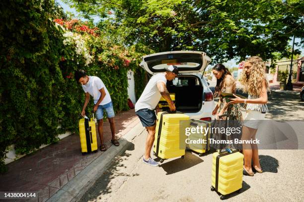 wide shot of family loading rental car with luggage while on vacation - car rental stockfoto's en -beelden