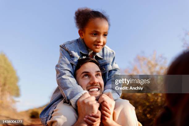 father holding his adoptive daughter on the shoulders - foster care stock pictures, royalty-free photos & images