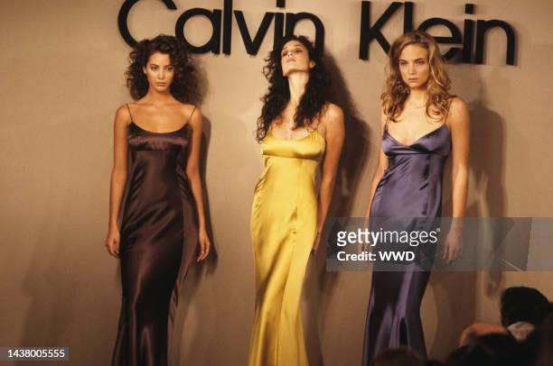 Three models wearing jewel-tone satin dresses on the runway from the RTW spring/summer '88 collection by Calvin Klein