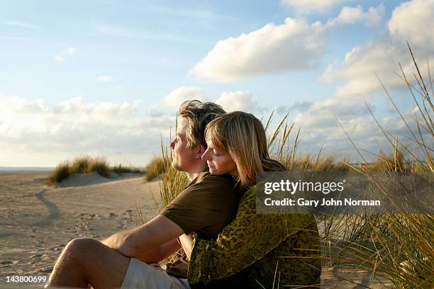 couple sitting embracing on beach - physical position photos et images de collection