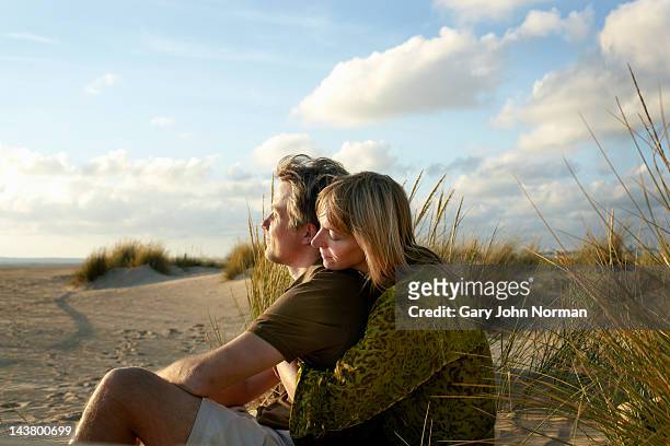couple sitting embracing on beach - embracing stock pictures, royalty-free photos & images