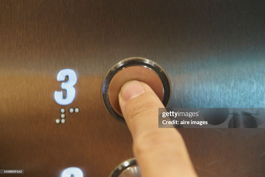 Unrecognizable person selecting a numbered 2 floor by pressing one of the elevator buttons with his finger