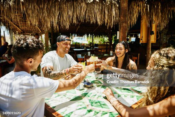 medium shot of smiling family toasting with drinks in beach cafe - strohgedeckte strandhütte stock-fotos und bilder