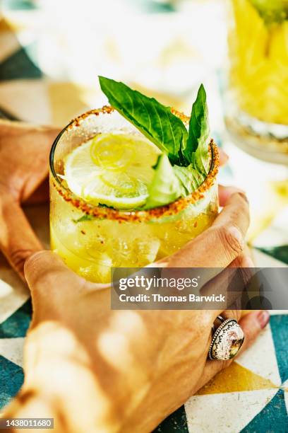 close up shot of womans hands holding margarita at table in beach cafe - margarita beach fotografías e imágenes de stock