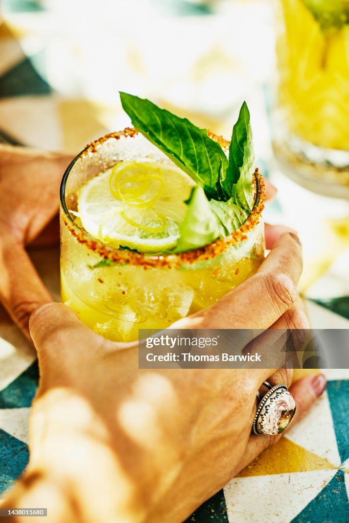 Close up shot of womans hands holding margarita at table in beach cafe