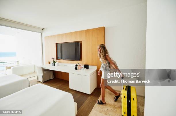 wide shot of smiling girl walking into hotel room with luggage - tv personality foto e immagini stock