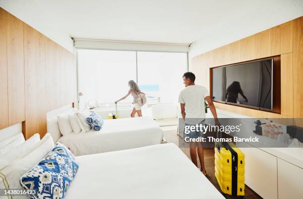 wide shot of siblings rolling luggage into hotel room while on vacation - habitación de hotel fotografías e imágenes de stock