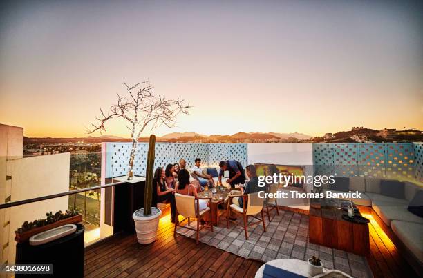 wide shot of families enjoying dinner on rooftop at resort during sunset - luxury family stock-fotos und bilder