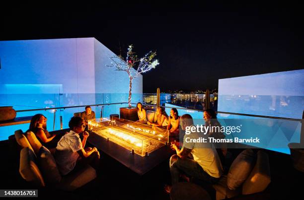 wide shot of families relaxing around fire pit on rooftop at resort - restaurant night ストックフォトと画像