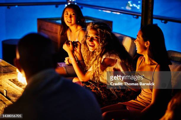 medium shot of smiling teenage girls relaxing around fire pit at resort - hot mexican girls stock-fotos und bilder