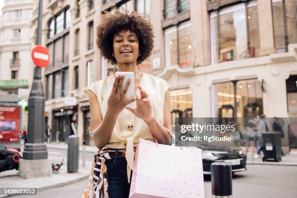 portrait of a young african american woman waiting a taxi after shopping - madrid shopping stock pictures, royalty-free photos & images