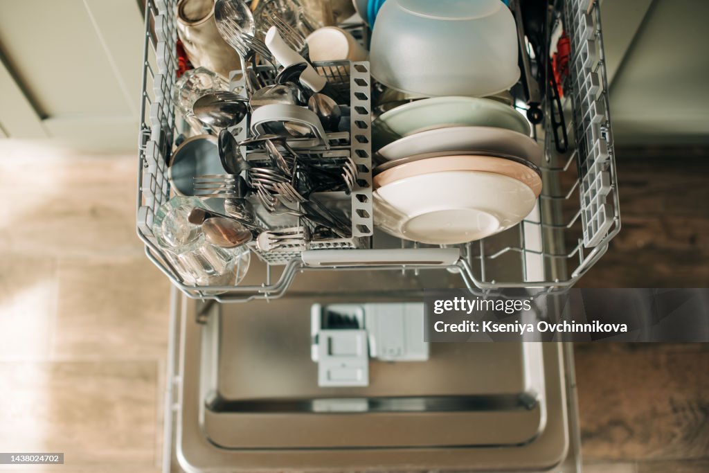 Open dishwasher with clean dishes in the white kitchen