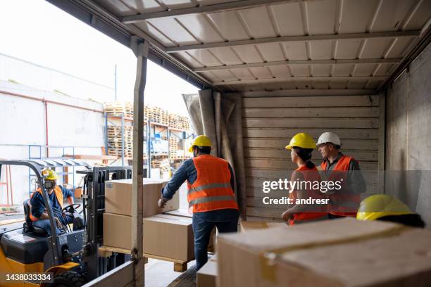 workers unloading packages from a truck while while working at a distribution warehouse - unloading stockfoto's en -beelden