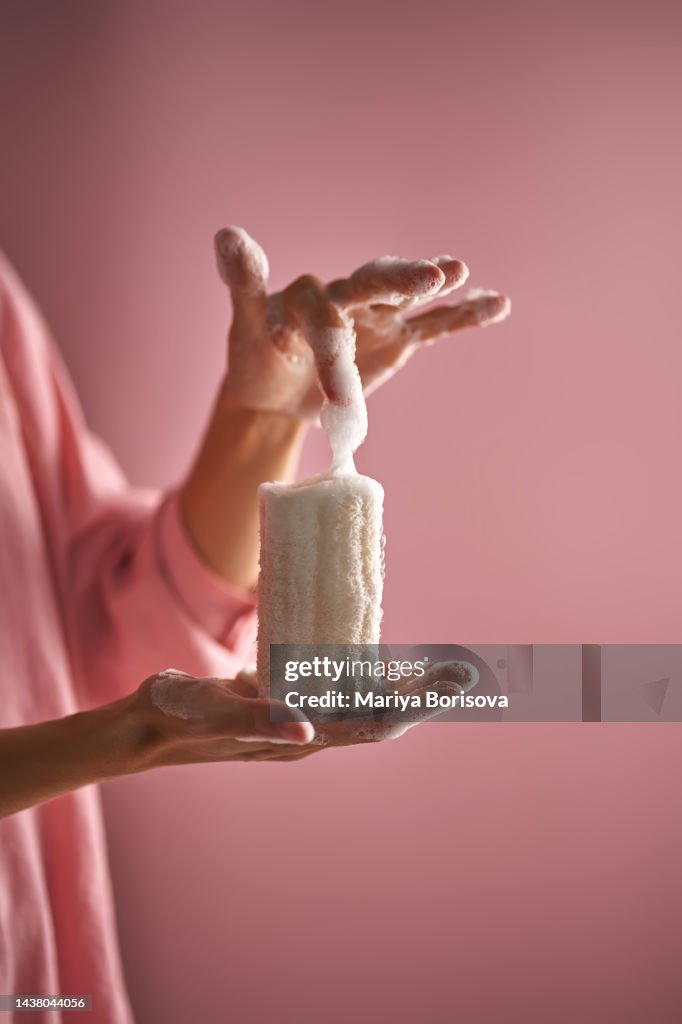 The girl in pink holds in her hand a natural loofah sponge in foam.