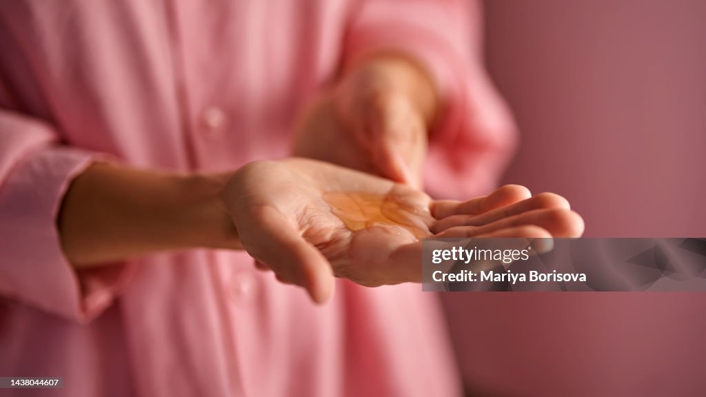 The girl in pink holds a gel cosmetic in her palm.