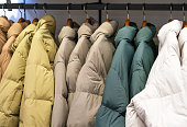 Multicolored winter down jackets hanging on hangers in the store close-up, side view.
