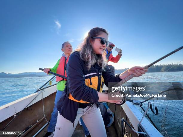 multiracial woman reeling in fish on boat with family helping - canadian pacific women stock pictures, royalty-free photos & images