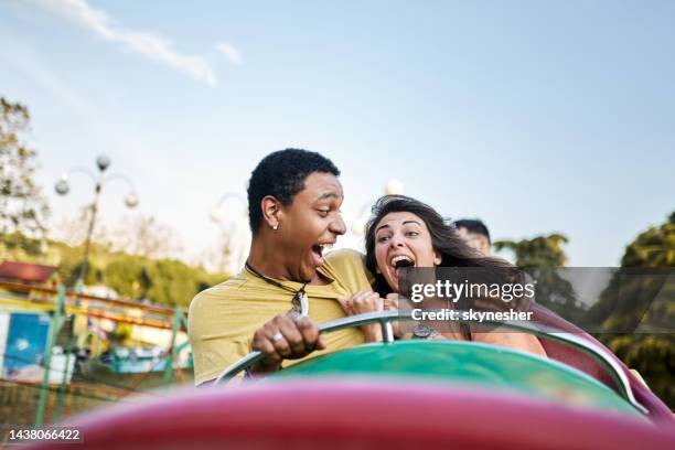 cheerful couple having fun while riding on rollercoaster at amusement park. - rollercoaster stock pictures, royalty-free photos & images