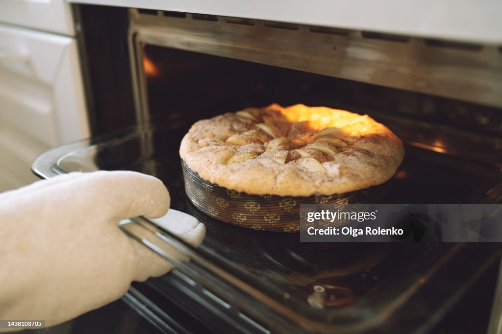 Potholder using for hot pie tray. Cropped hands in potholder gloves removing hot sweet pie from oven in the kitchen